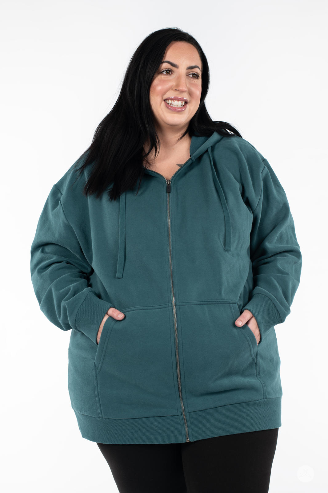 Smiling woman wearing teal On the Move Zip Hoodie by SweetLegs Canada with hands in front pockets on white background