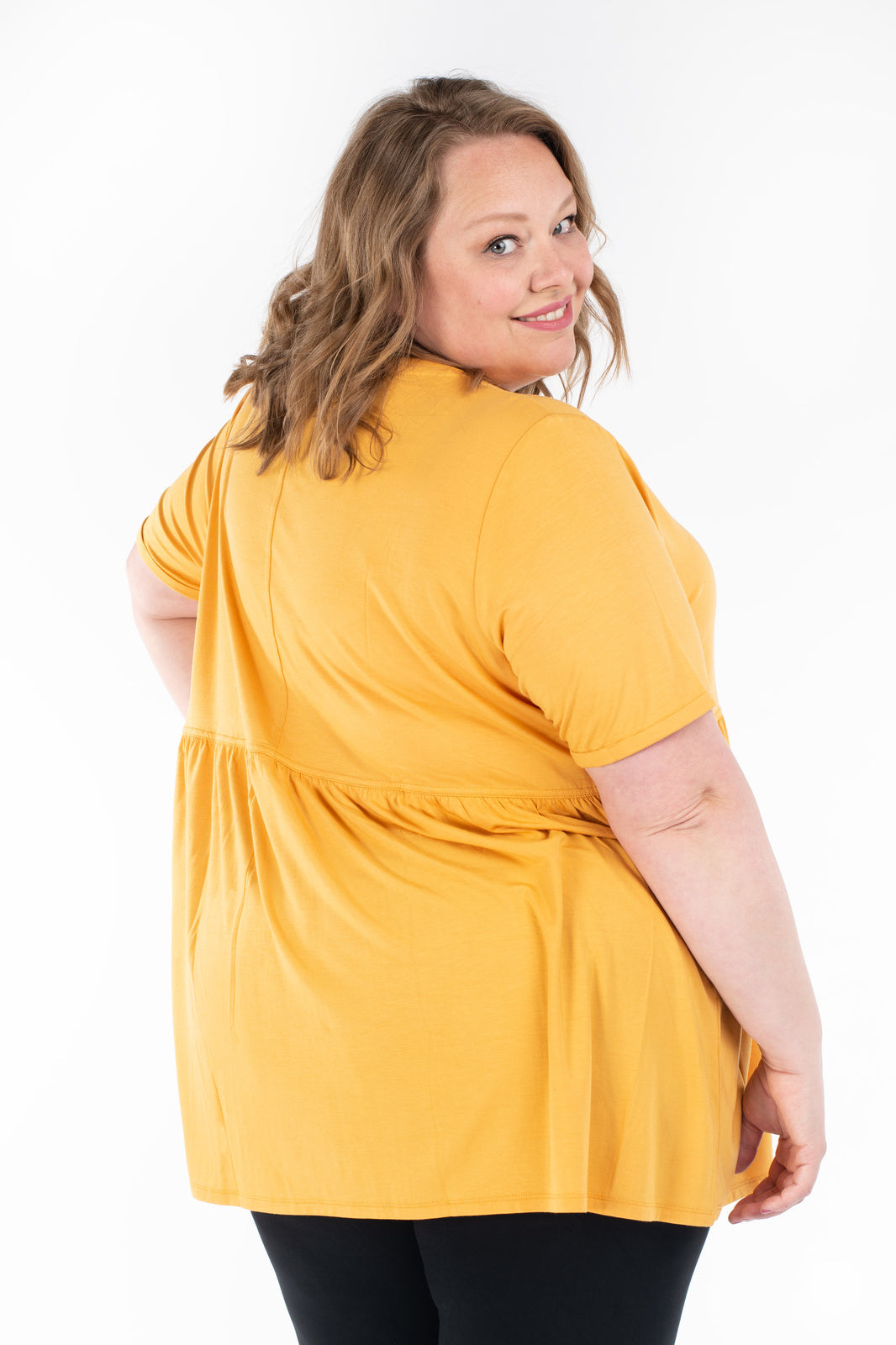 Plus-size woman smiling wearing yellow Babydoll Tee by SweetLegs Canada showing back view on white background