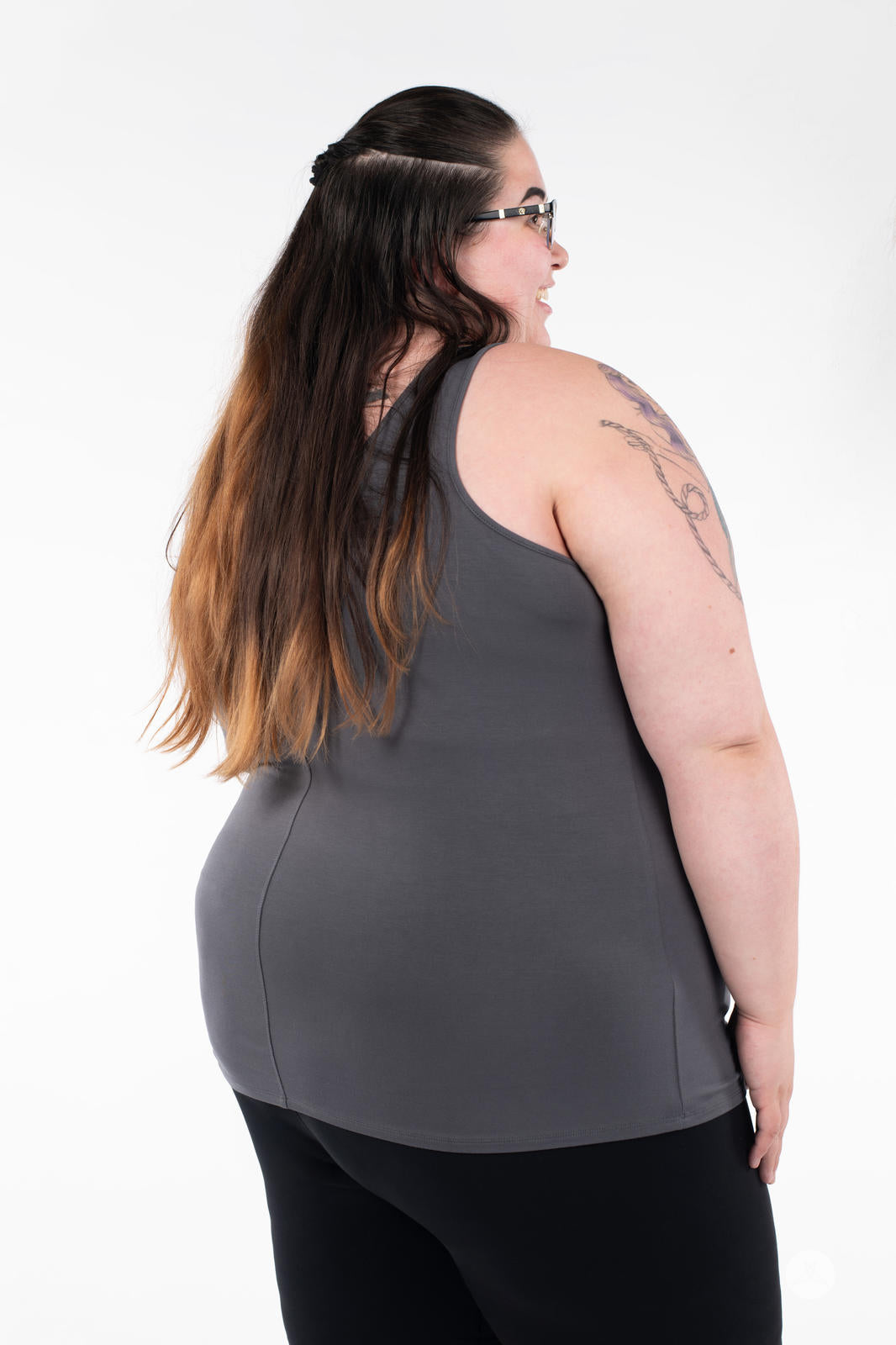 Plus-size woman modeling SweetLegs Canada Classic Tank in grey, shown from side back with black pants on white background