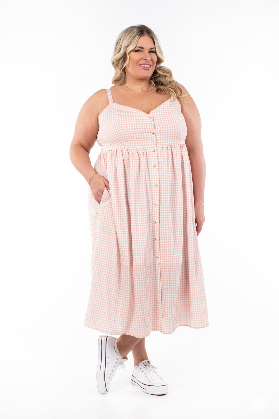 Plus-size model wearing SweetTops Gingham Dress in soft pink and white with buttons and side pockets, smiling confidently