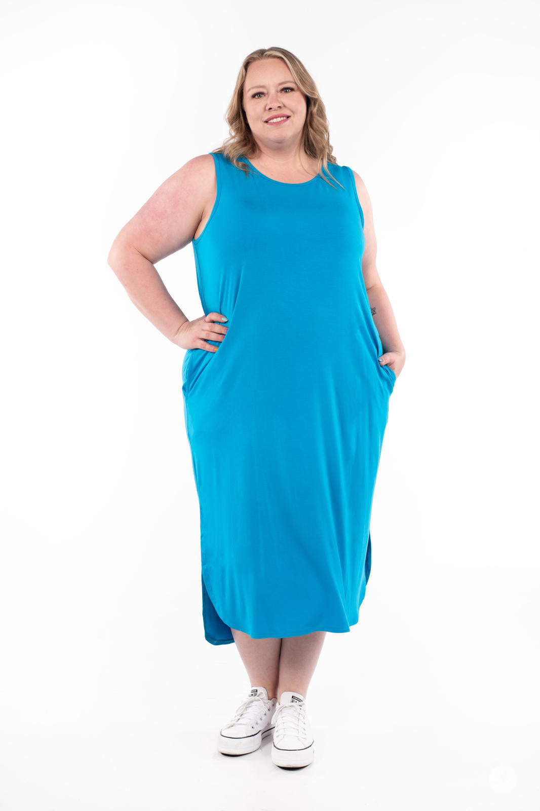 Plus-size woman wearing bright blue Sleeveless Tank Dress by SweetTops with pockets and white sneakers on white background