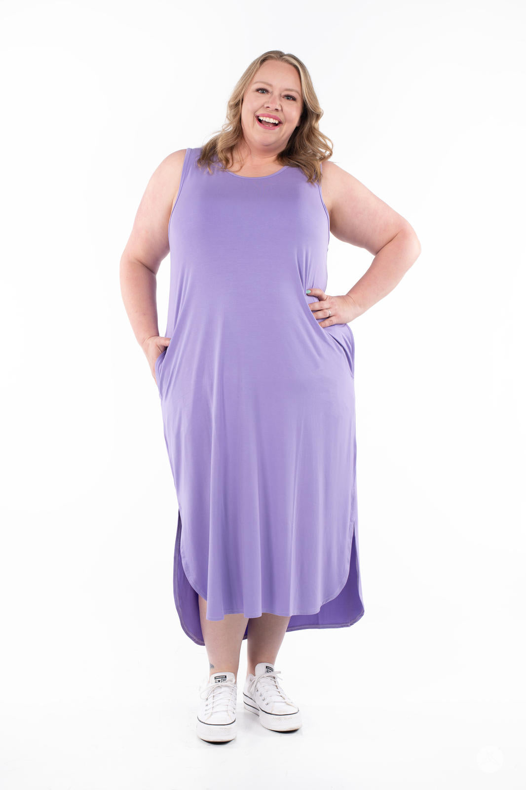 Plus-size woman smiling wearing SweetTops Sleeveless Tank Dress in lavender with pockets and sneakers on white background