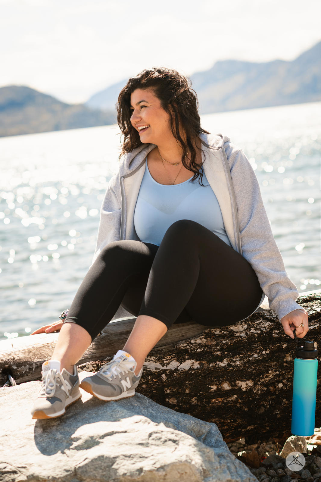Woman sitting on log by water wearing black Free Motion Crops by Athleisure SweetLegs collection outdoors