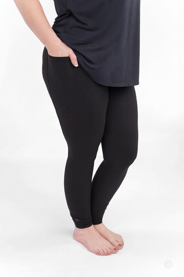 Curvy model wearing SweetLegs Black Pocket Leggings with hands in side pockets standing barefoot side view