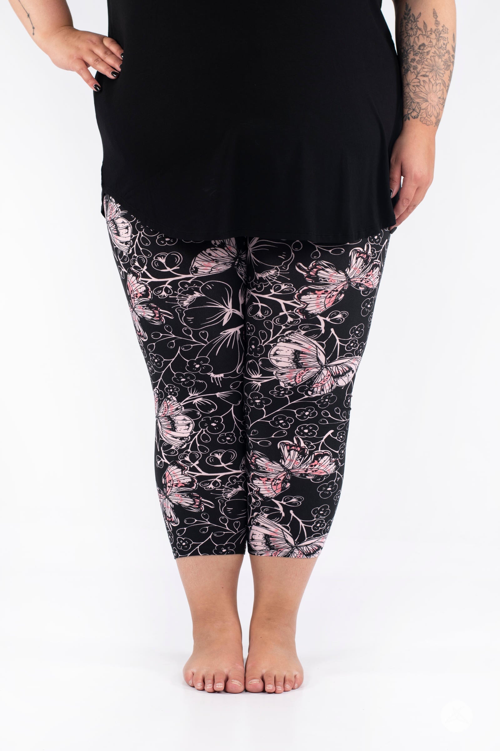 Plus-size model wearing SweetLegs Butterfly Bliss 2.0 Crops with pink butterfly pattern and black top on white backdrop