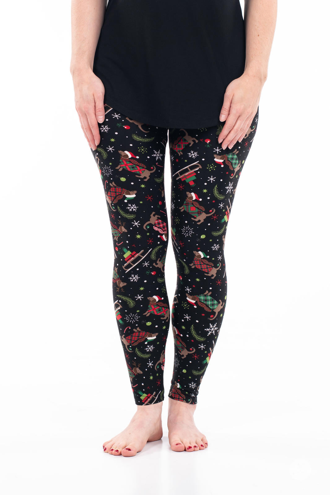 Front view of adult wearing SweetLegs Happy Pawlidays leggings with Christmas Dachshunds and festive sleighs on black background