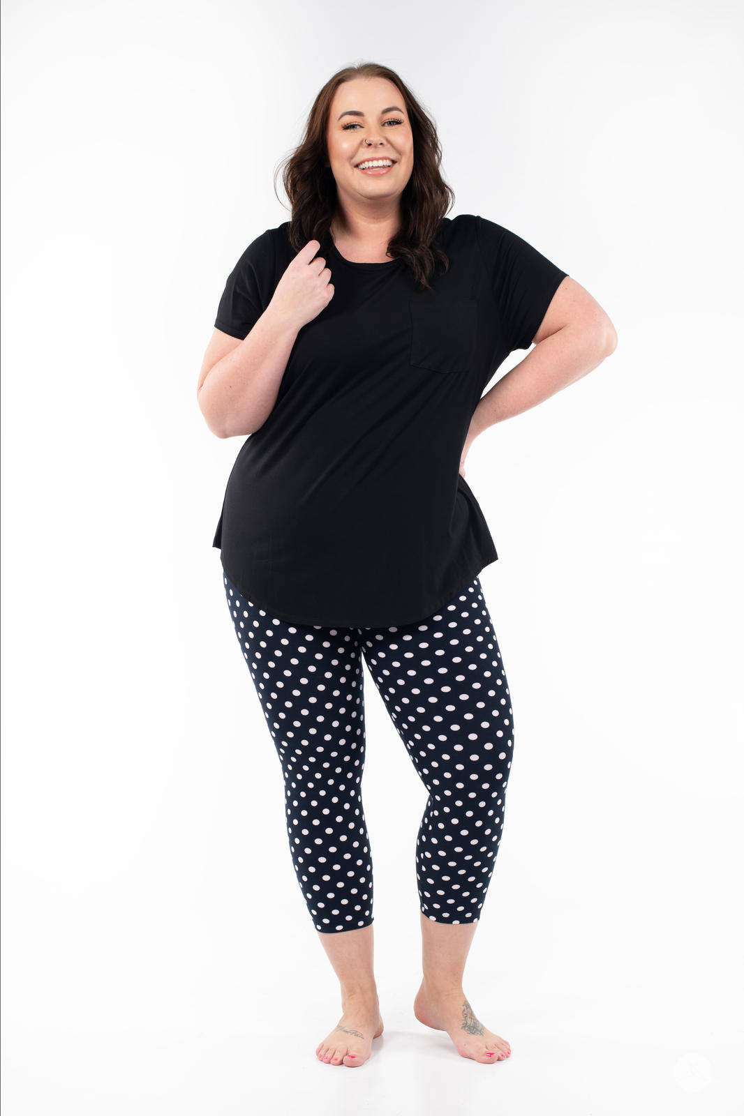 Woman smiling wearing SweetLegs Get Spotted Crops navy polka dot leggings with black top on white background