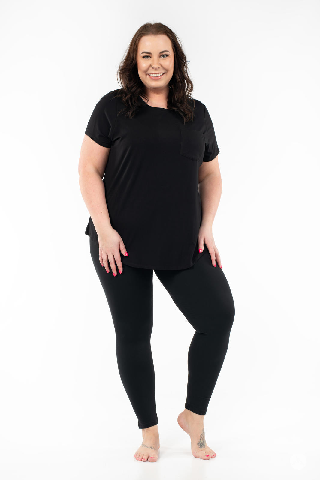 Smiling woman wearing SweetLegs Black Licorice leggings with black short sleeve top standing barefoot on white background