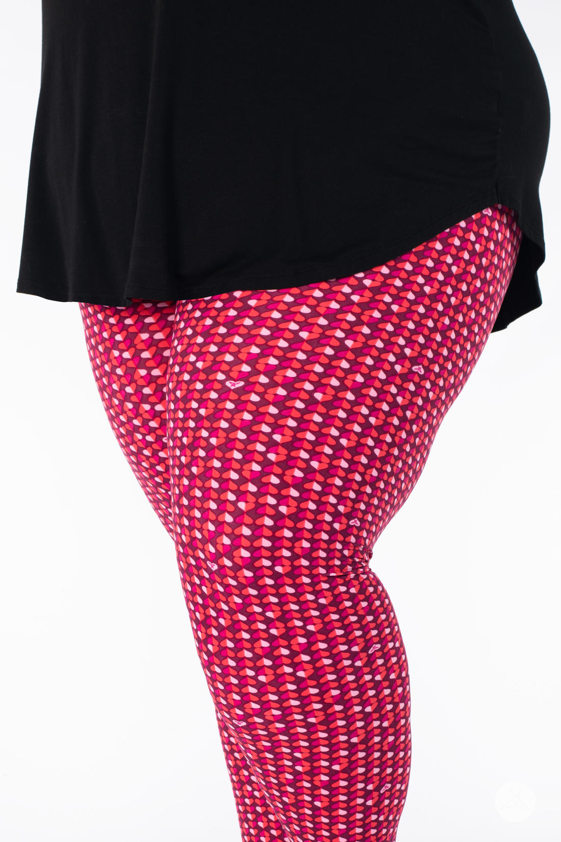 Close-up side view of SweetLegs Lovesick leggings with bold duo-colored pink and purple heart pattern worn with black top