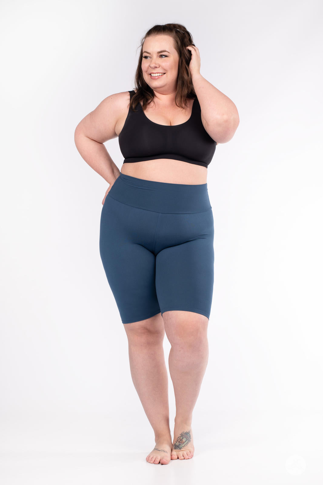 Plus-size model smiling while wearing SweetLegs Solid High-Waisted Biker Shorts in deep blue with a high-rise fit