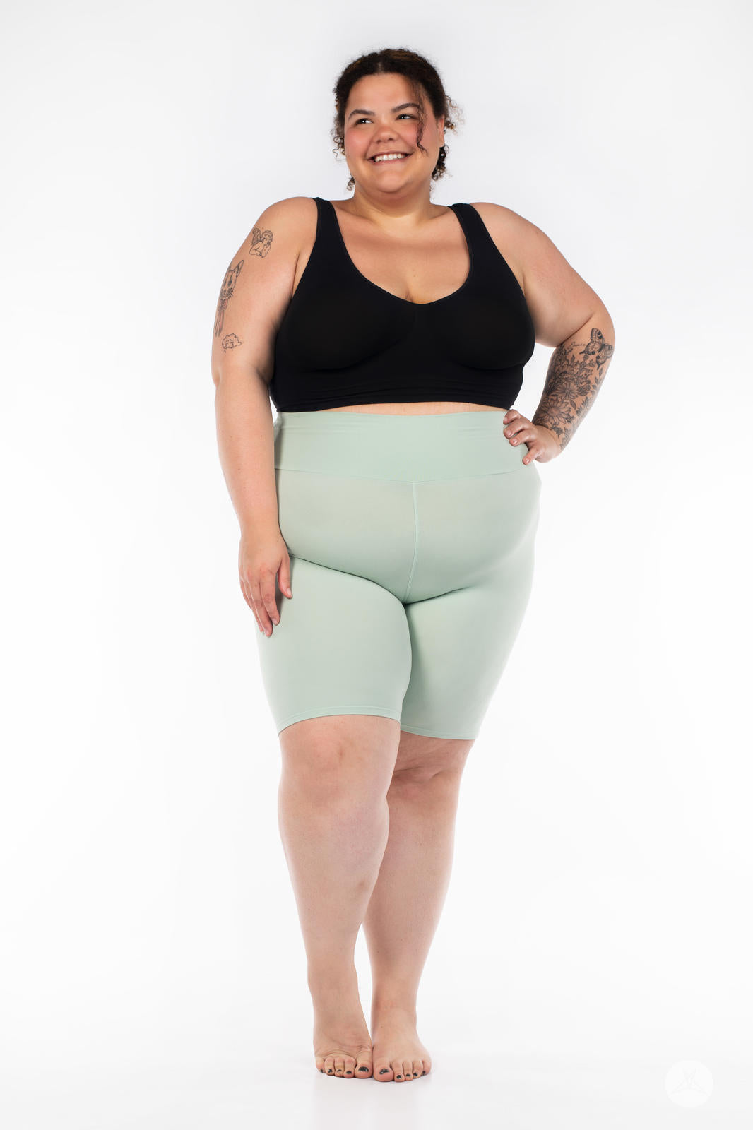 Plus-size model smiling and wearing SweetLegs Solid High-Waisted Biker Shorts in soft mint with a comfortable waistband