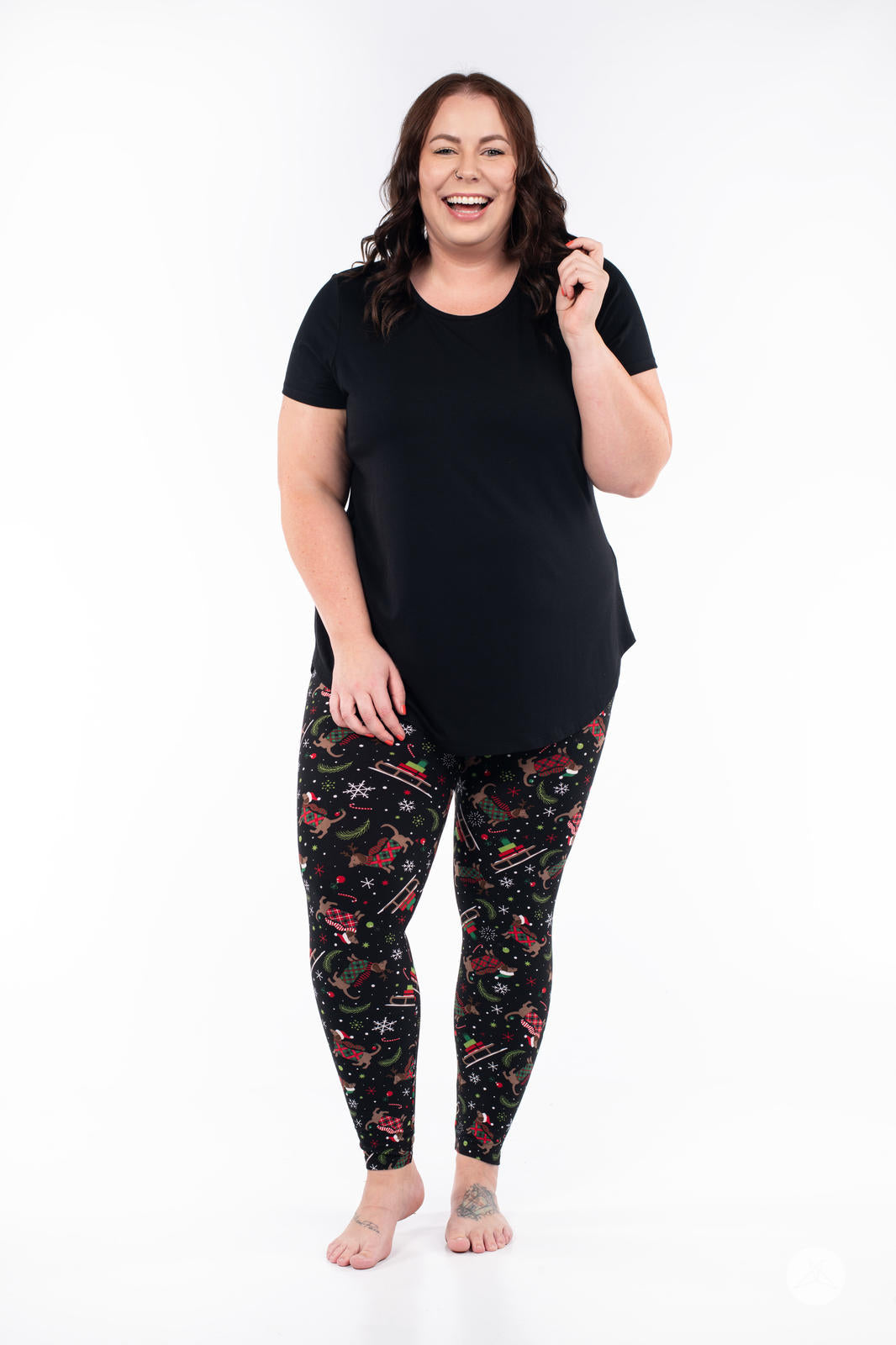 Plus-size model wearing SweetLegs Happy Pawlidays leggings with festive Dachshunds and holiday sleighs on black background