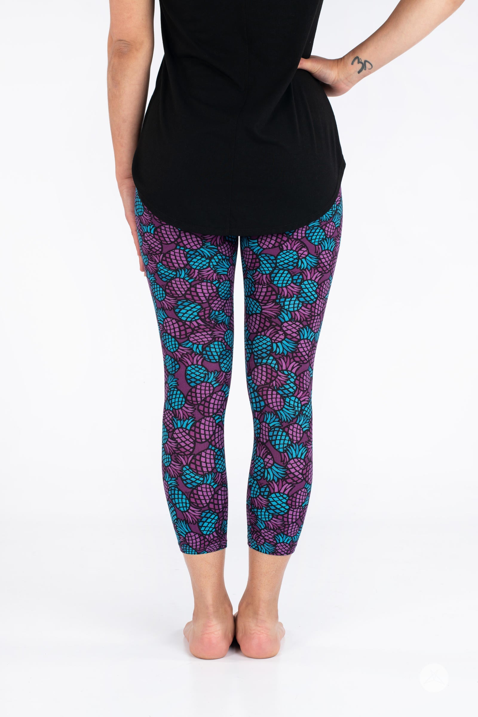 Rear view of SweetLegs Razzle Dazzle Crops in purple and teal pineapple pattern cropped leggings on model