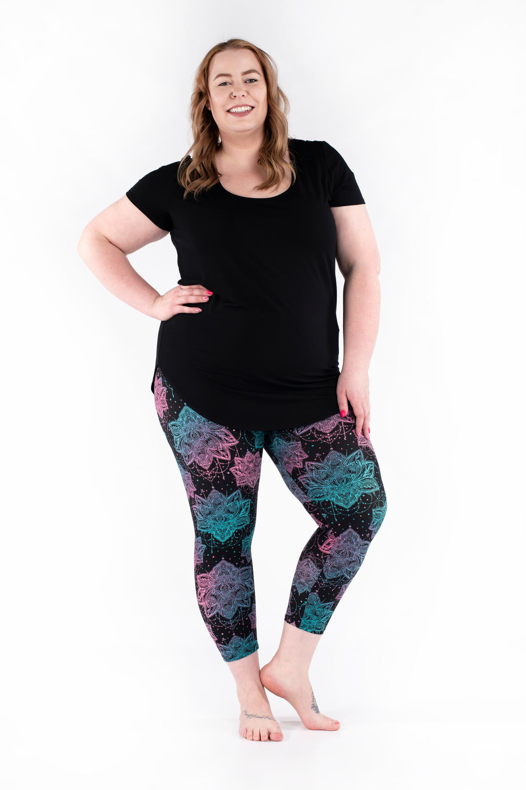 Plus-size model wearing SweetLegs Everafter Crops with teal and pink floral geometric designs on black background, front view