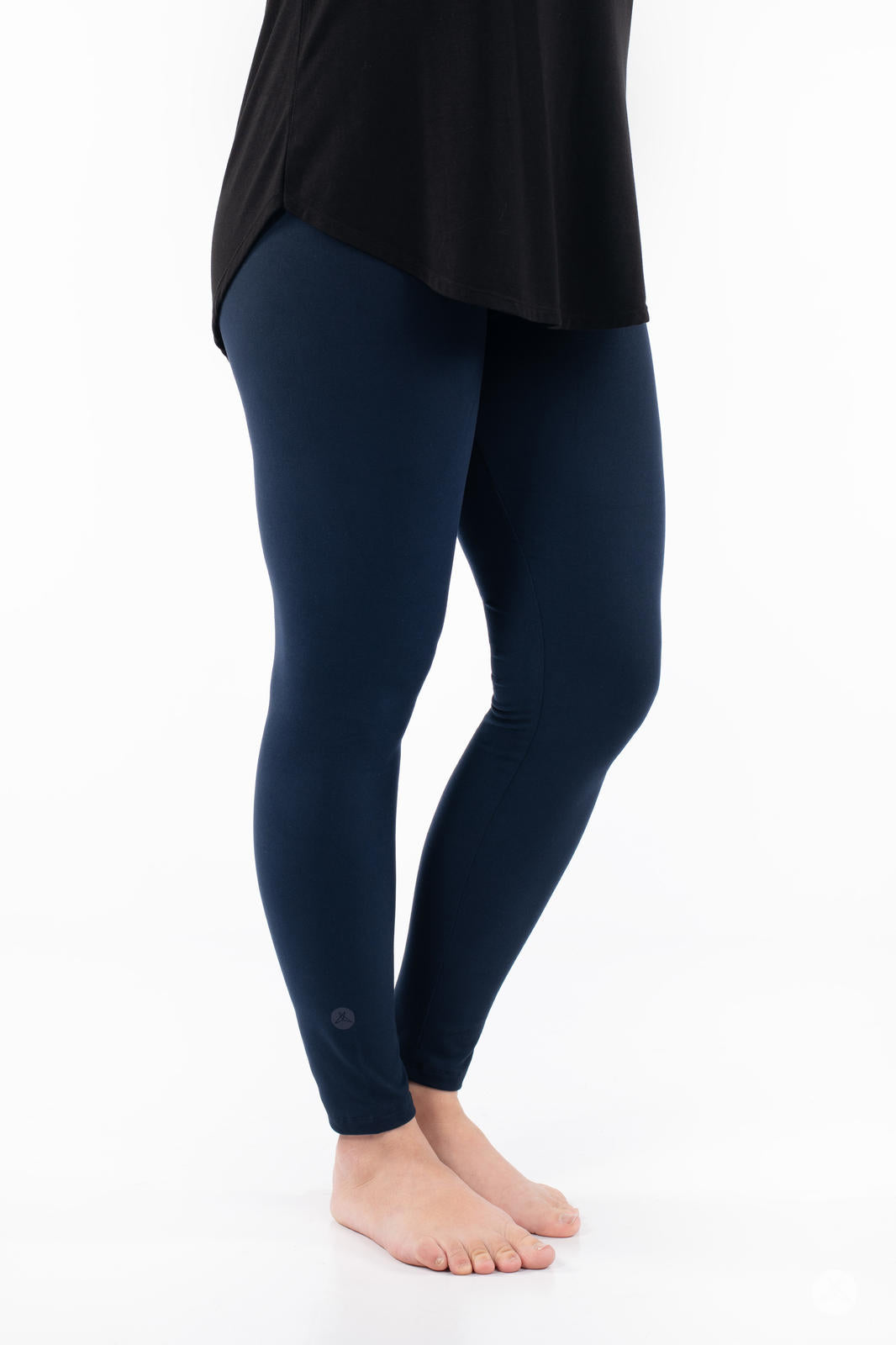 Side view of model wearing Navy leggings by SweetLegs paired with black top standing barefoot on white background