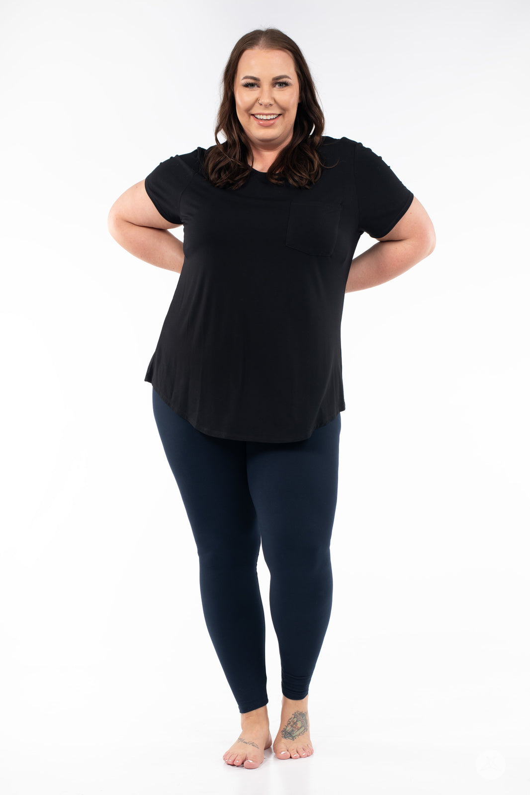 Smiling woman wearing Navy leggings by SweetLegs paired with black T-shirt standing barefoot on white background