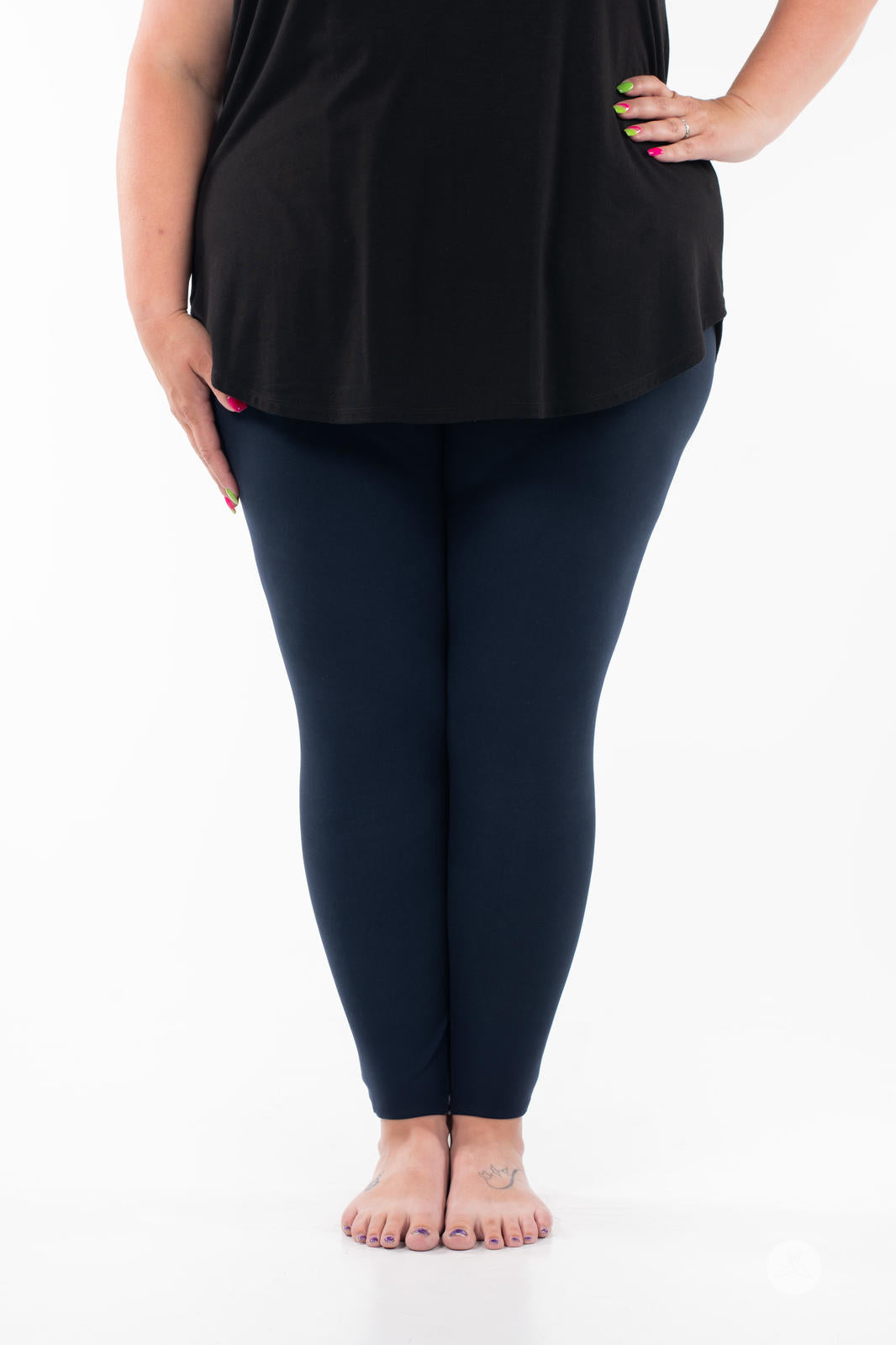 Plus-size model wearing Navy leggings by SweetLegs paired with black top standing barefoot on white background