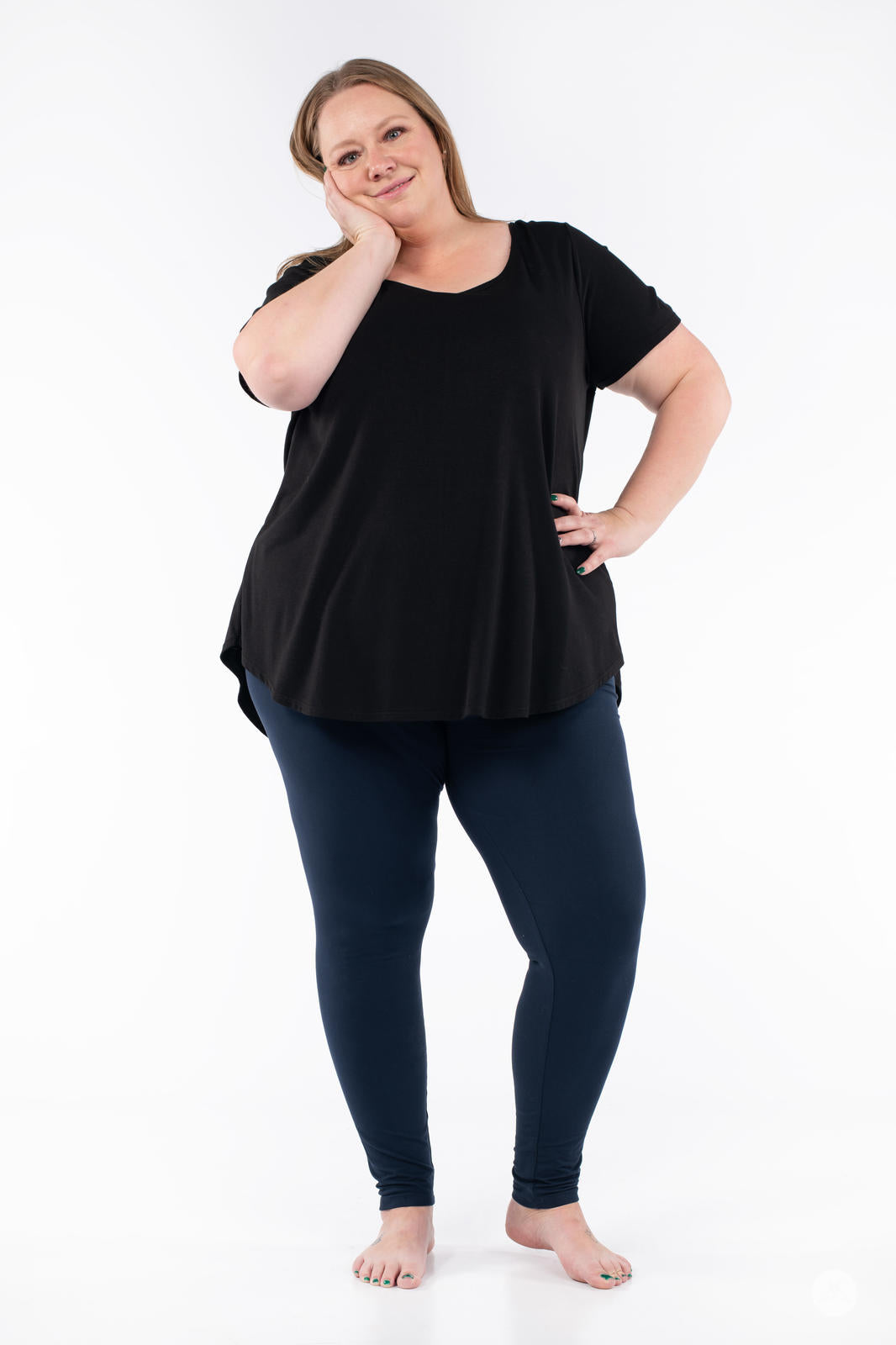 Plus size model standing barefoot wearing Navy leggings by SweetLegs paired with black short-sleeve top on white background