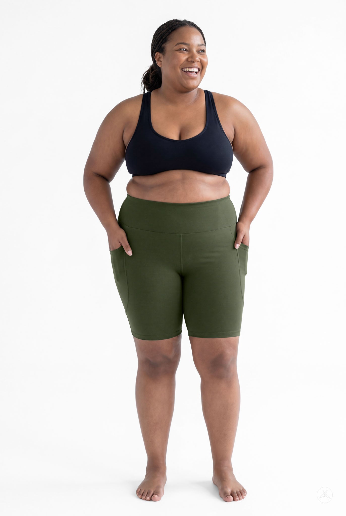 Plus size model wearing SweetLegs Cedar High-Waisted Pocket Biker Shorts in green with black sports bra smiling front view