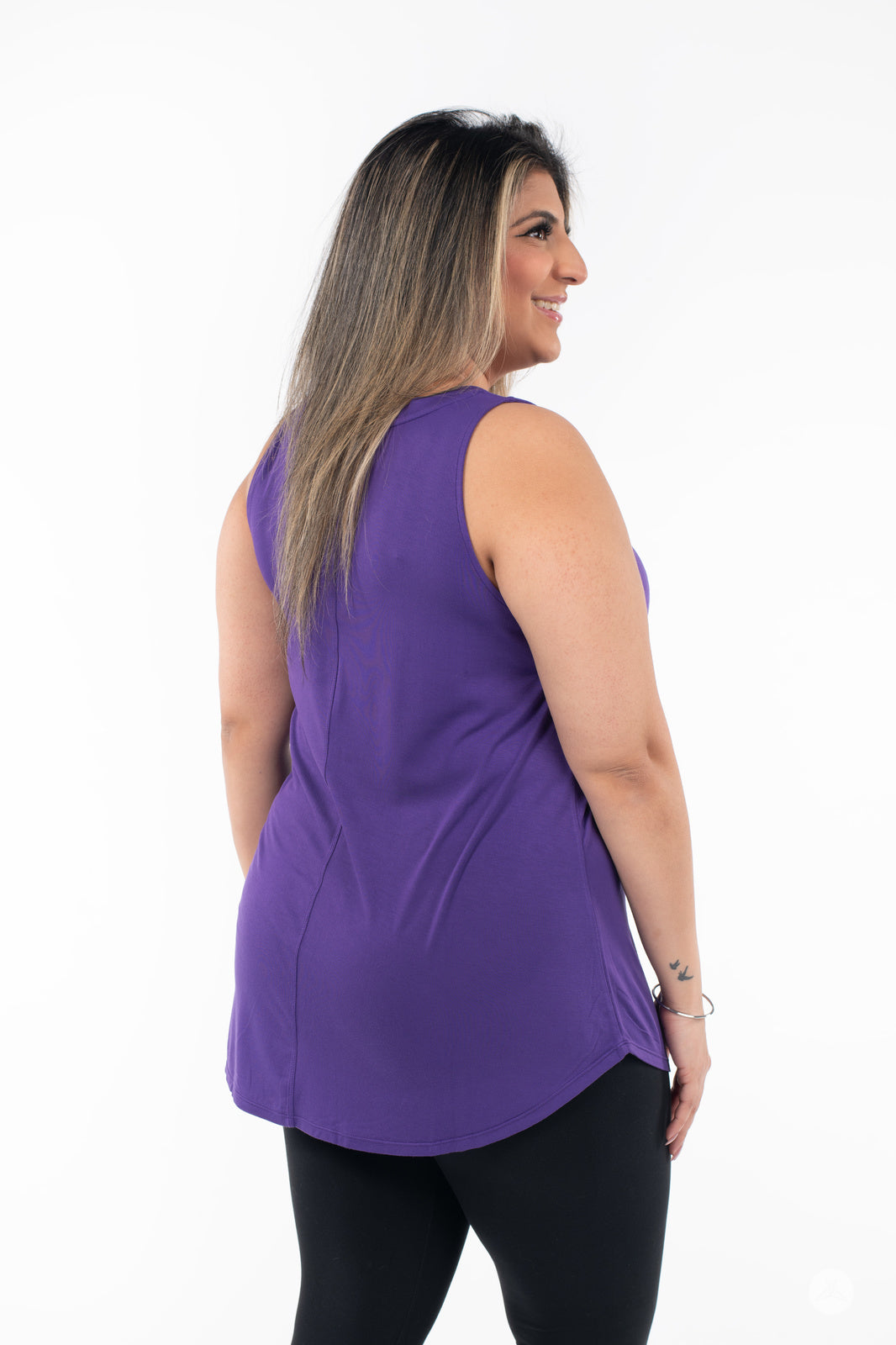 Plus-size model showing back of SweetTops High Neck Swing Tank in purple with black leggings on white background