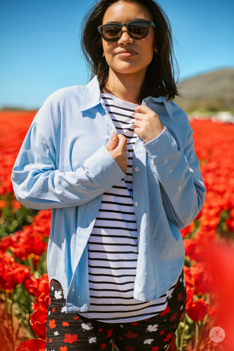 Woman wearing SweetTops Classic Linen Shirt in soft blue over striped top posing in vibrant red flower field