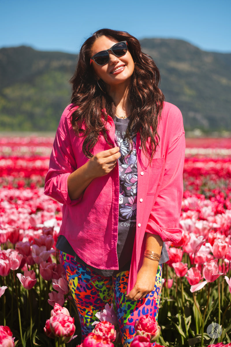 Woman in SweetTops Classic Linen Shirt in bright pink standing in colorful tulip field with mountains in background