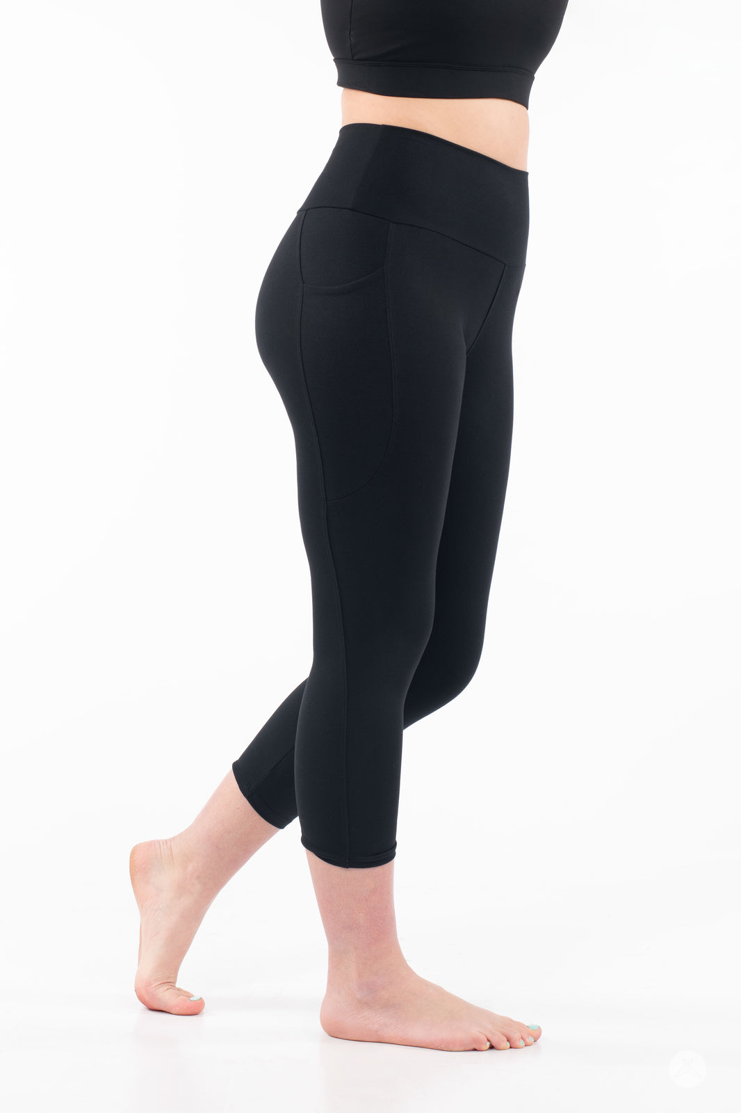 Side view of barefoot woman wearing black SweetLegs High-Waist Pocket Crops showing pocket detail on white background