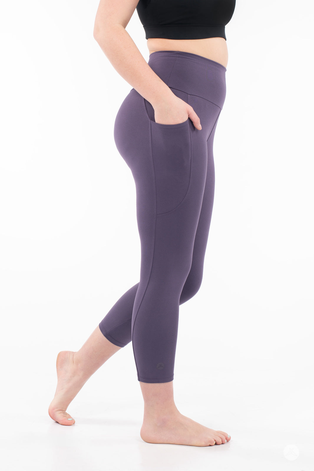 Side view of woman wearing plum SweetLegs High-Waist Pocket Crops with hand in pocket barefoot on white background