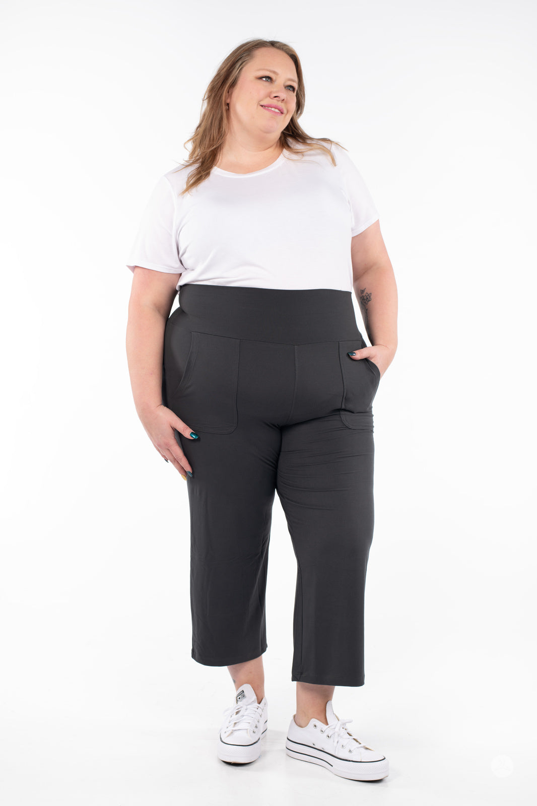 Plus-size model wearing SweetLegs High-Waist Wide Leg Crops in black with pockets and white sneakers, front view.