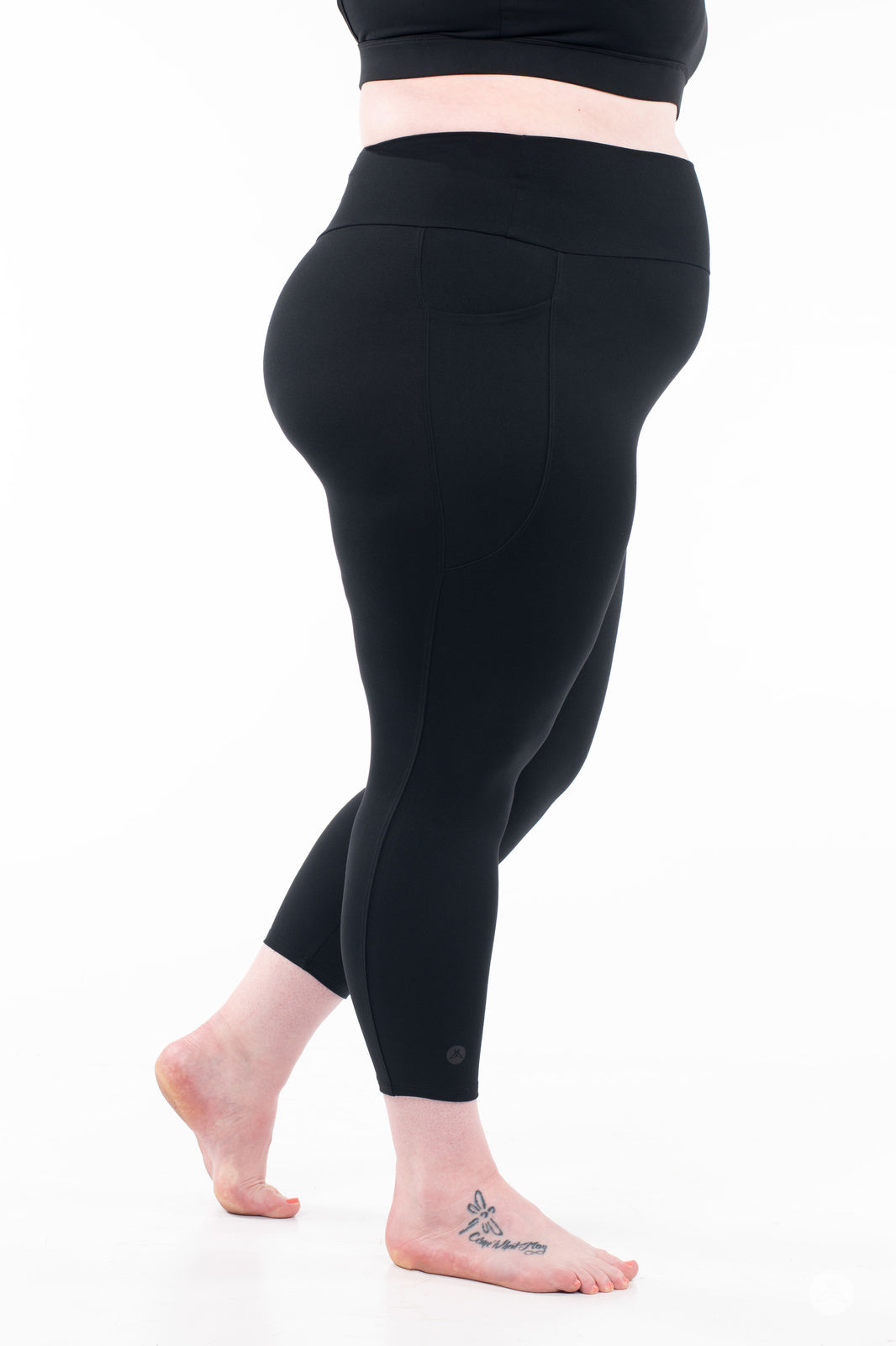 Side view of plus-size model barefoot wearing black SweetLegs High-Waist Pocket Crops standing on white background