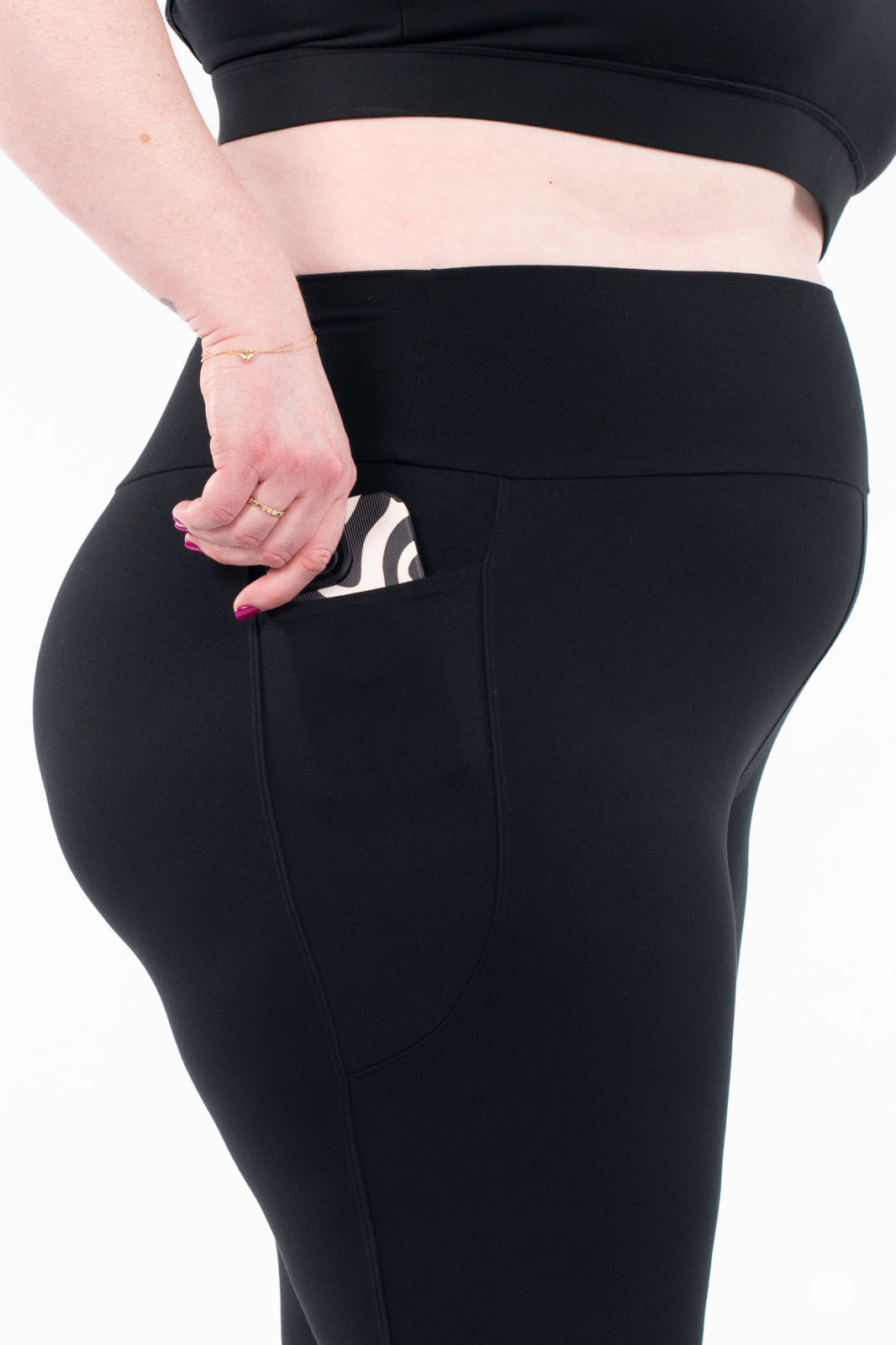 Plus-size model wearing black SweetLegs High-Waist Pocket Crops showing side pocket with hand placing phone inside
