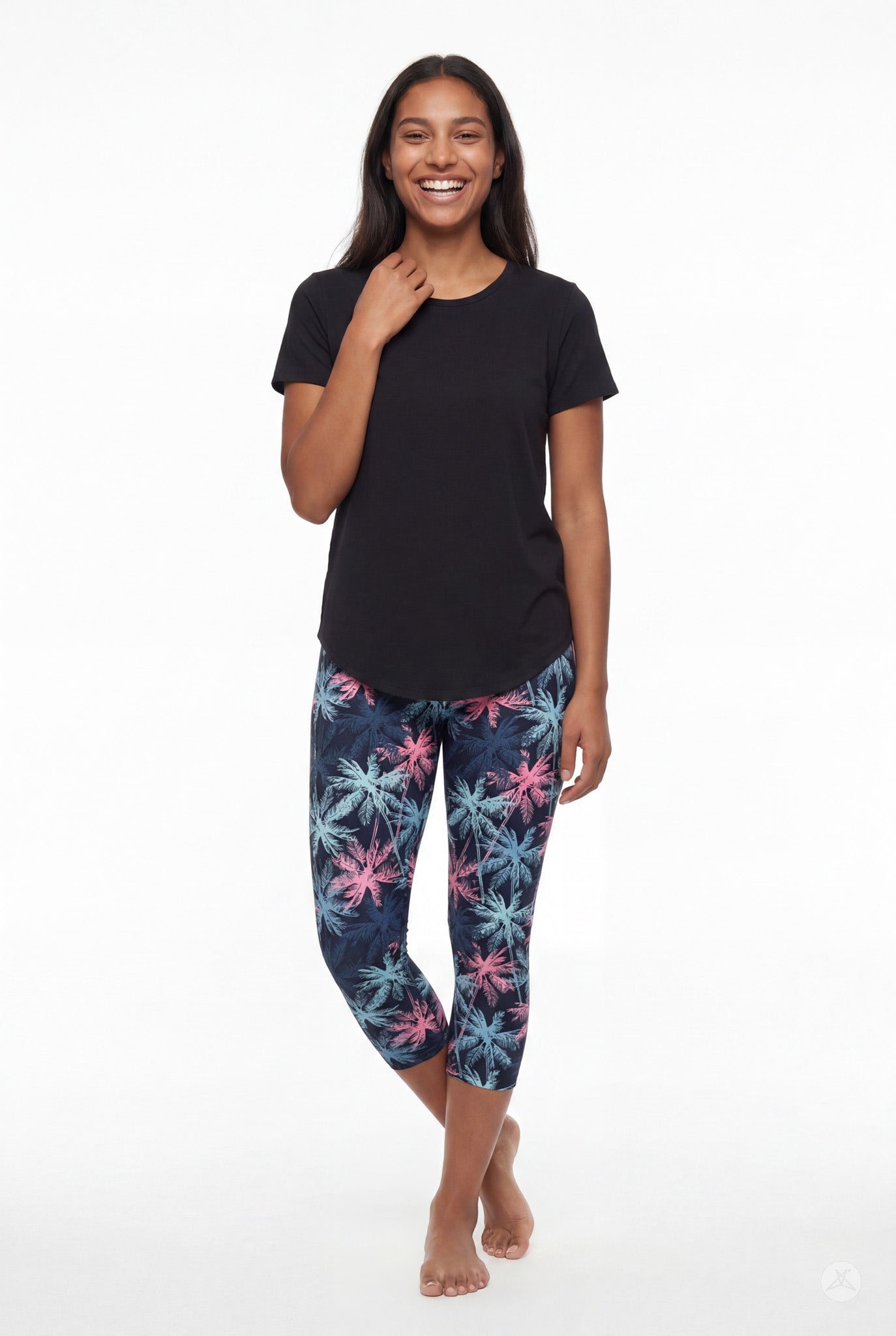 Smiling woman wearing SweetLegs Tiki Nights Crops with colorful palm tree print and black short sleeve top standing barefoot