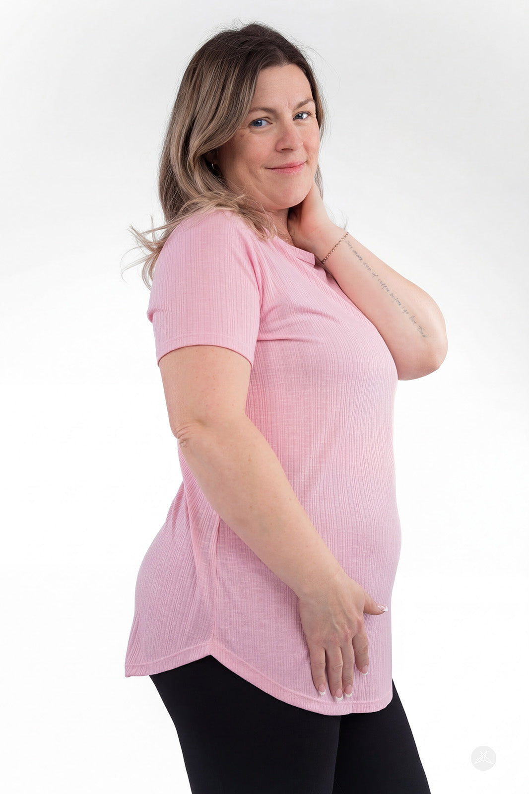 Plus-size woman wearing light pink The Soft Ribbed Tee by SweetLegs Canada with ribbed fabric and curved hem side angle view