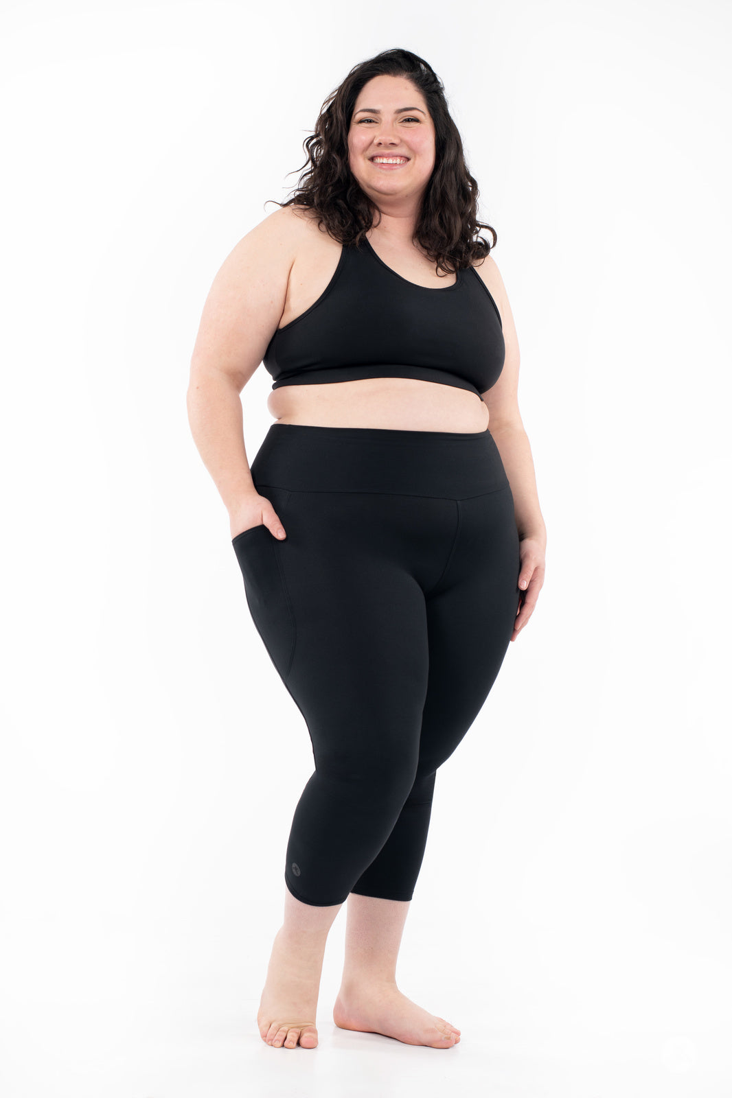 Smiling plus-size woman wearing black SweetLegs High-Waist Pocket Crops with hands in pockets on white background