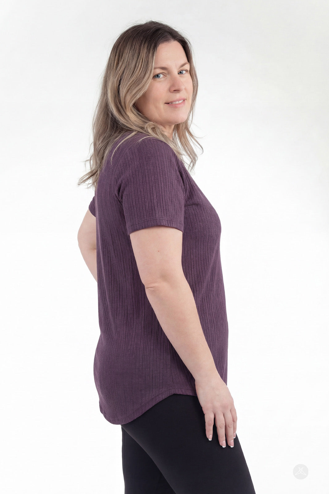 Side profile of woman wearing purple The Soft Ribbed Tee by SweetLegs Canada with rib-knit fabric and curved hem