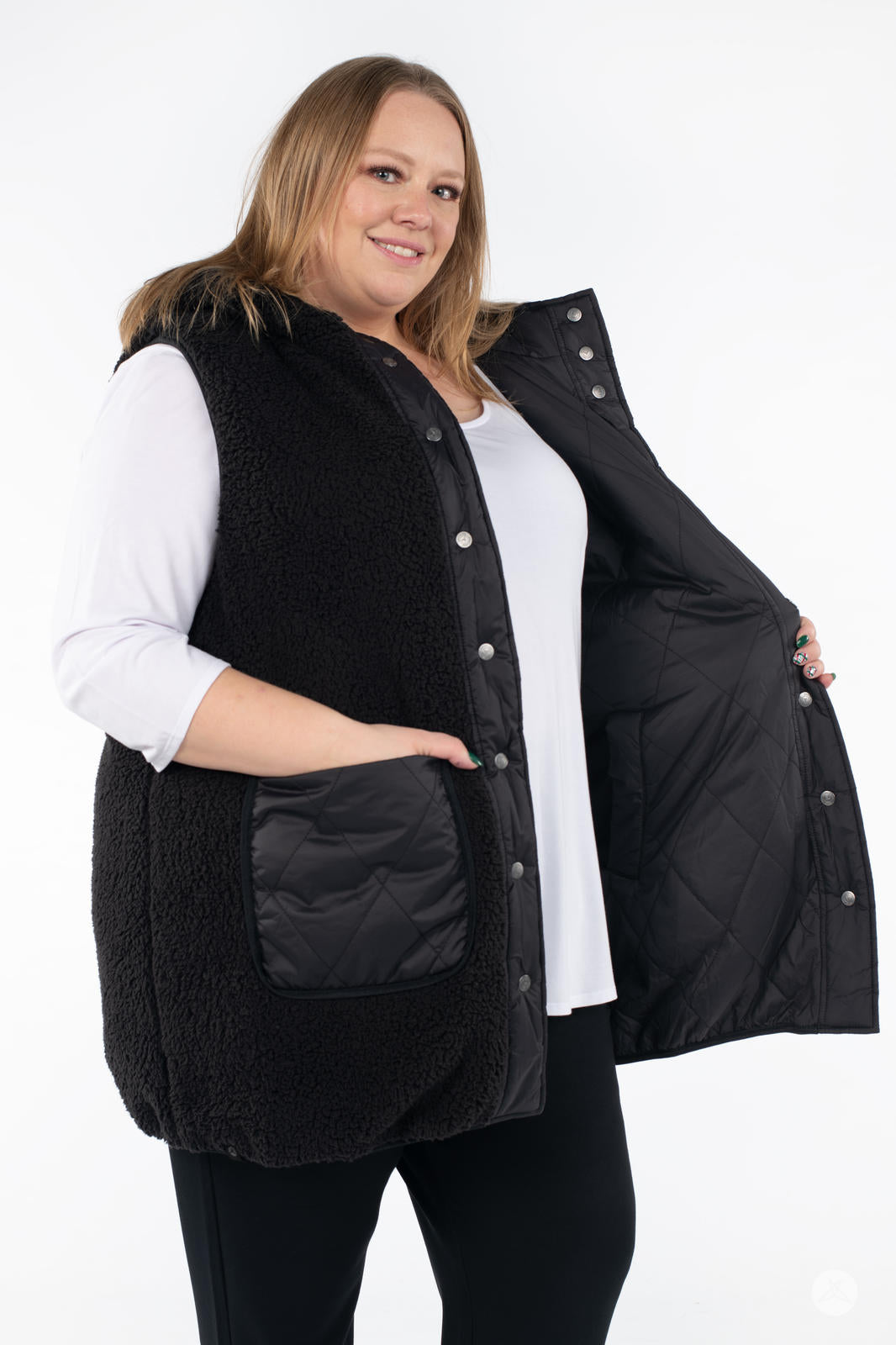 Plus-size woman showing inside lining of black SweetLegs Canada Reversible Quilted Sherpa Vest with hand in pocket