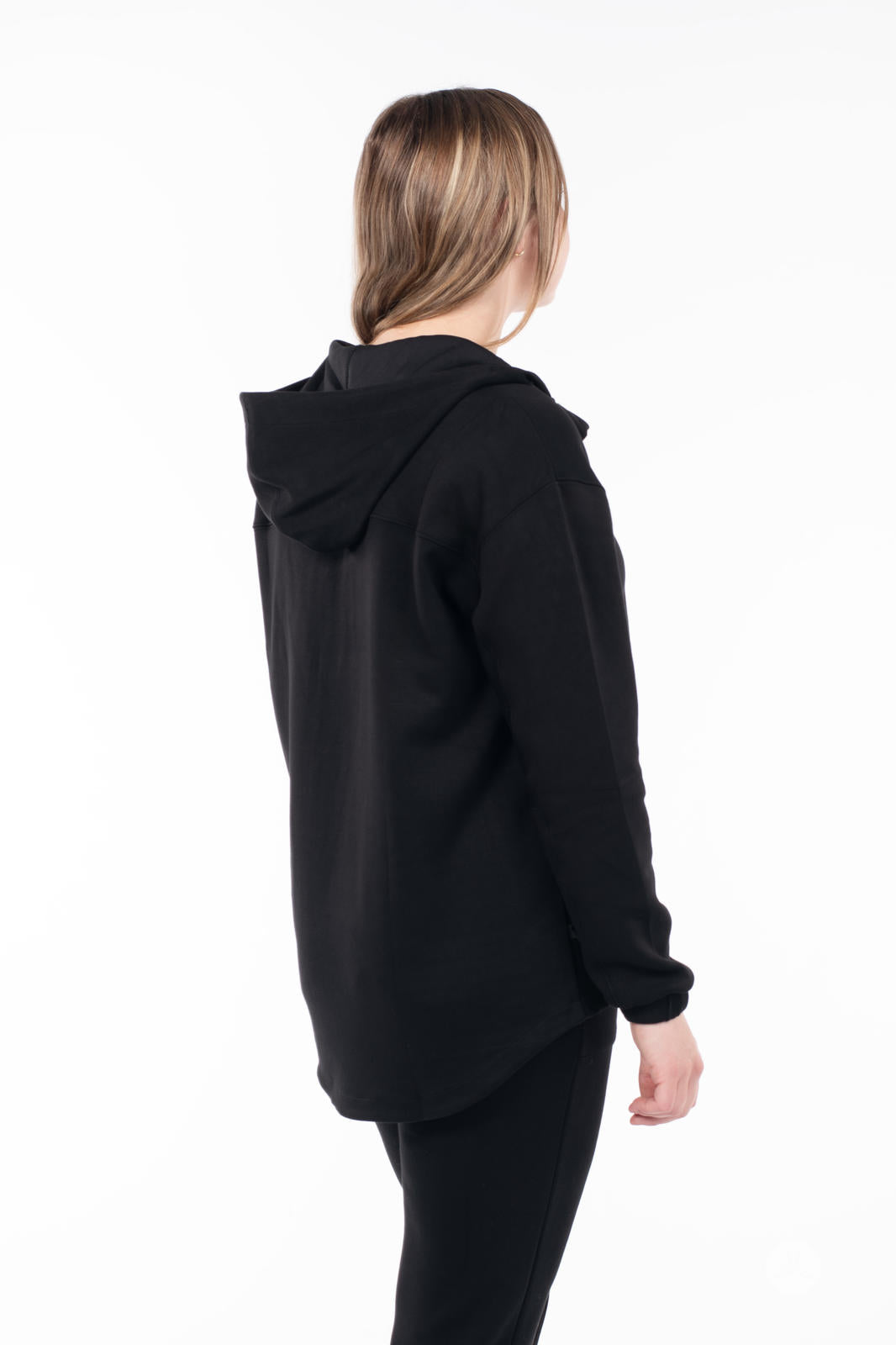 Back view of woman wearing black SweetTops All Day Hoodie with hood and relaxed fit on white background