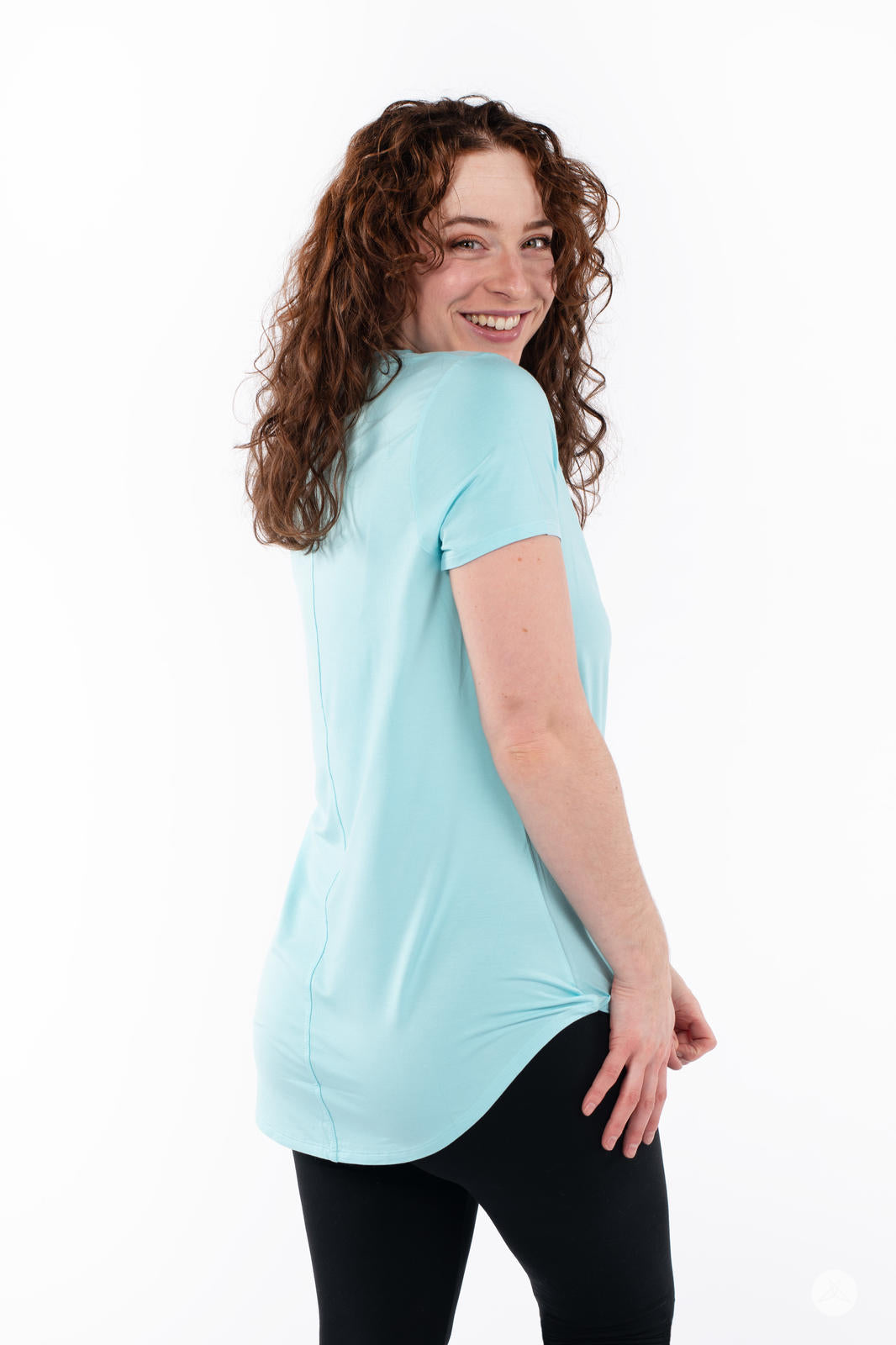 Woman smiling wearing SweetTops Crew Neck Pocket Tee in light blue showing back and side details with black pants