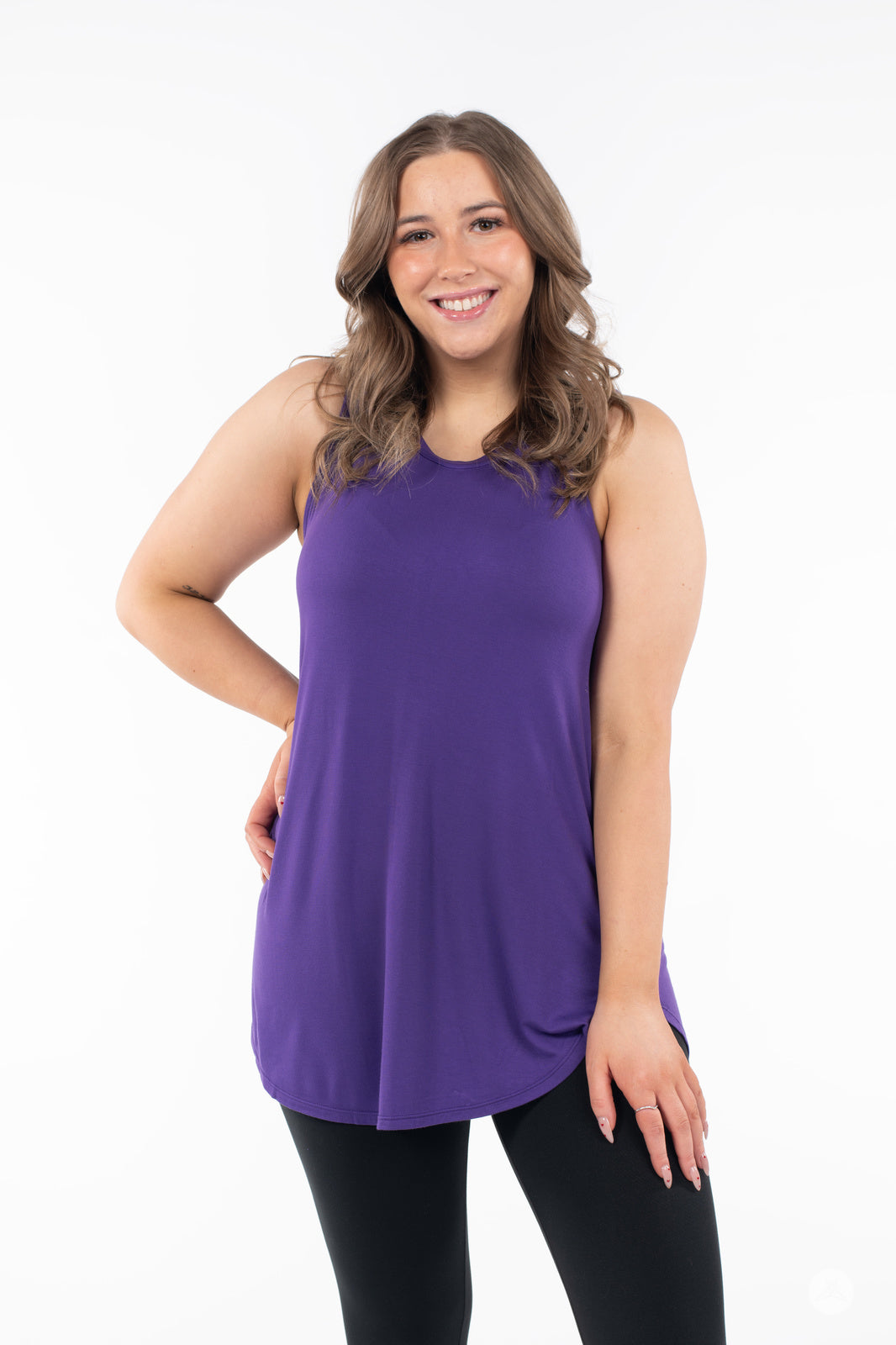 Smiling woman wearing SweetTops High Neck Swing Tank in vibrant purple paired with black leggings on white background