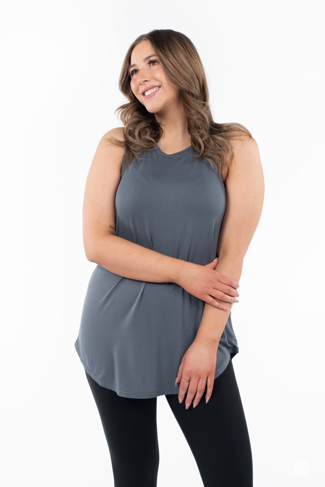 Smiling woman wearing SweetTops High Neck Swing Tank in muted blue paired with black leggings on white background