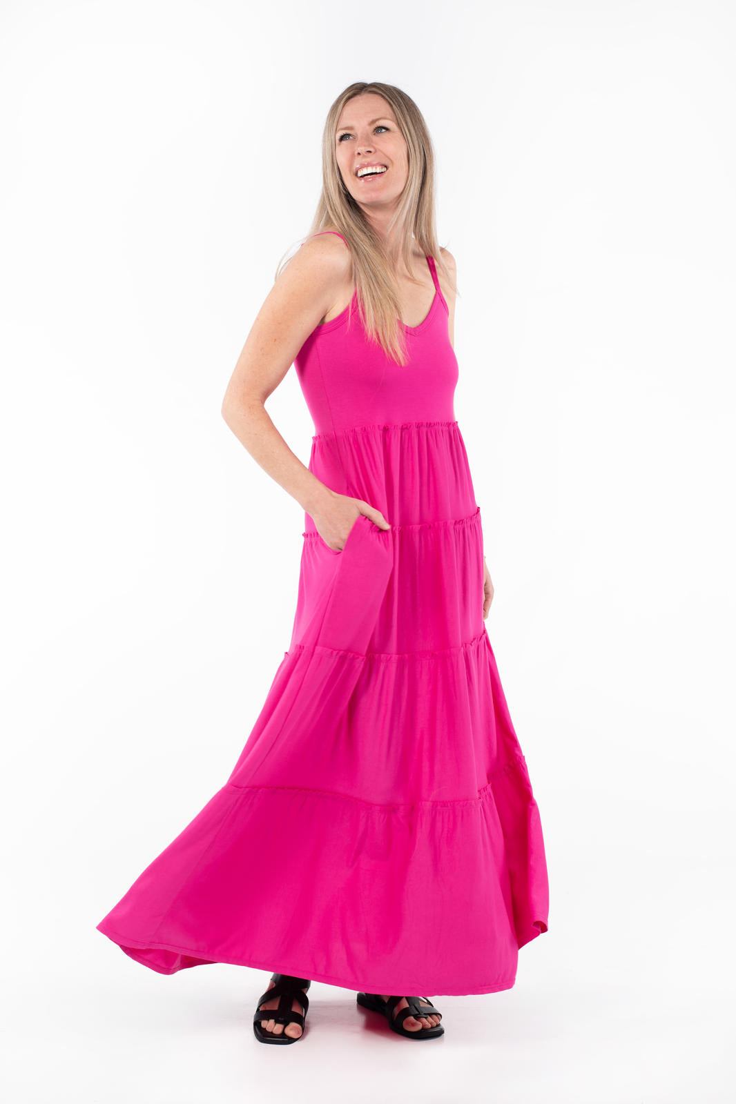 Woman wearing SweetTops The Summer Tiered Dress in bright pink with adjustable straps and flowing tiered maxi skirt pockets visible