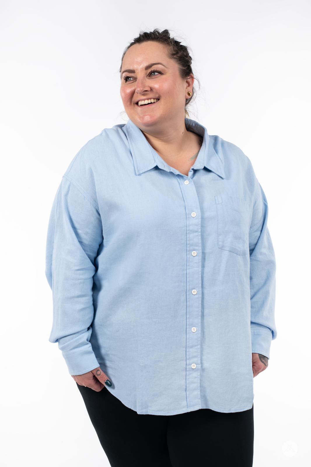 Plus-size model smiling wearing SweetTops Classic Linen Shirt in soft blue with relaxed fit and chest pocket on white background