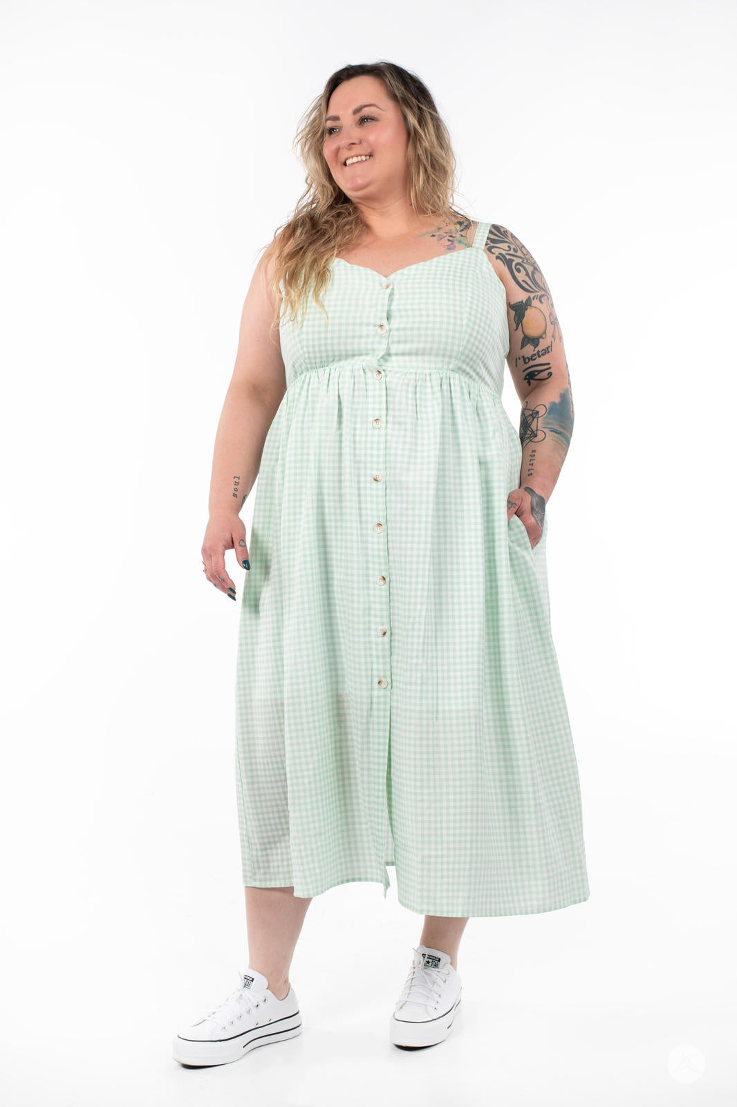 Plus-size model smiling and wearing SweetTops Gingham Dress in light green with button front and side pockets on white background