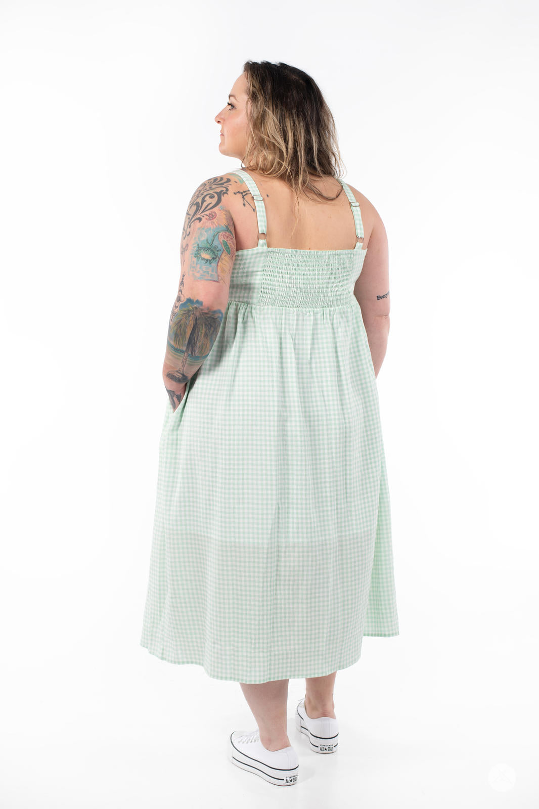 Plus-size model facing away wearing SweetTops Gingham Dress in light green with adjustable straps and side pockets visible