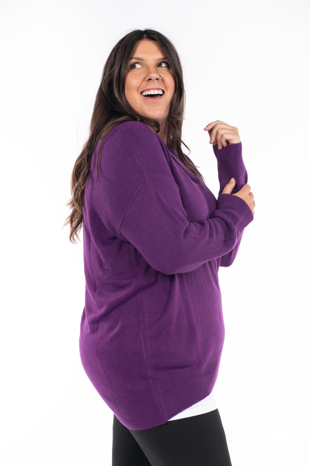 Woman wearing SweetTops Soft Knit V-Neck Sweater in rich purple with relaxed fit and ribbed details, smiling looking sideways