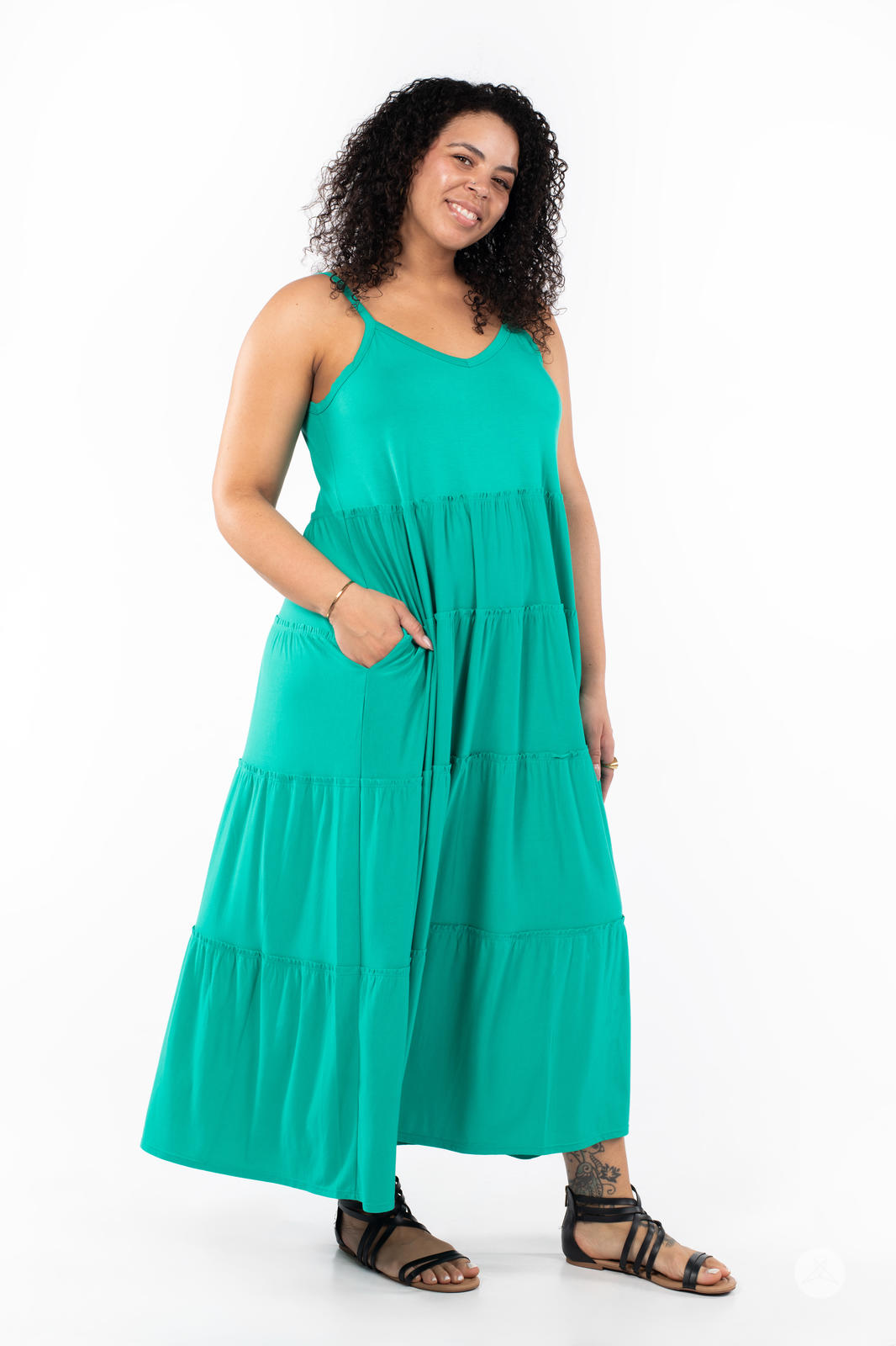 Smiling woman with curly hair wearing SweetTops The Summer Tiered Dress in green with pockets and adjustable straps