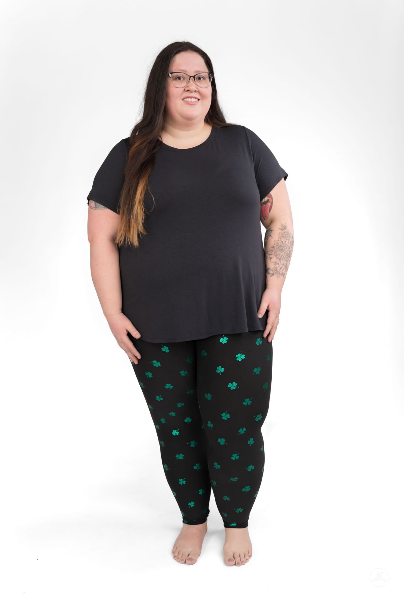 Plus size woman wearing Lucky Glow leggings with scattered emerald shamrocks by SweetLegs against white background
