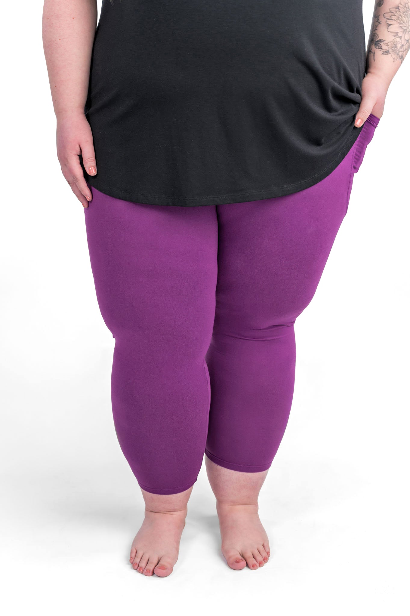 Plus size woman barefoot wearing sweetlegs Deep Plum Pocket Crops with black top and hands in pockets on white background