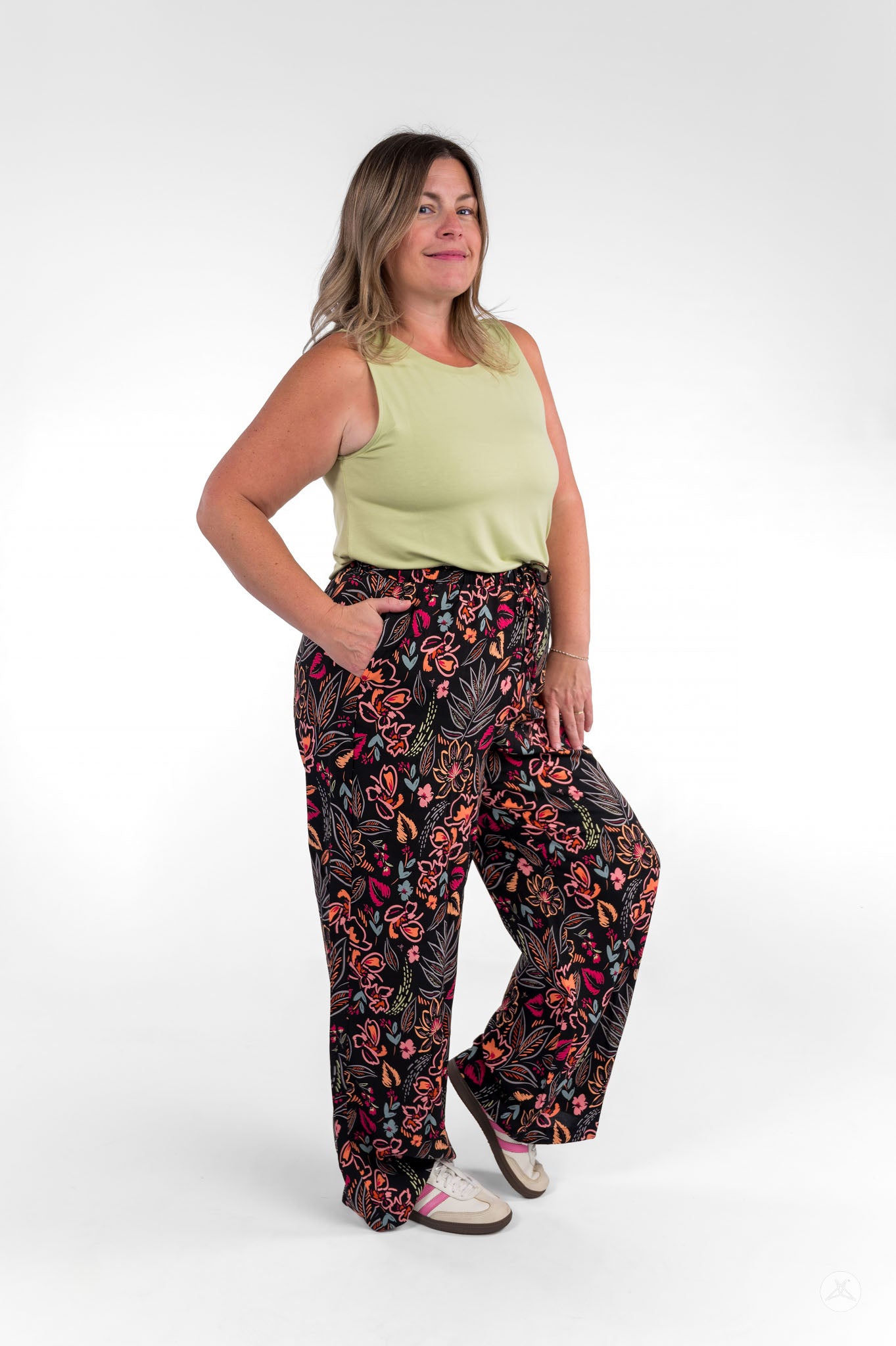 Woman wearing sweetlegs Breeze Wide-Leg Pant with colorful floral print paired with light green sleeveless top on white background