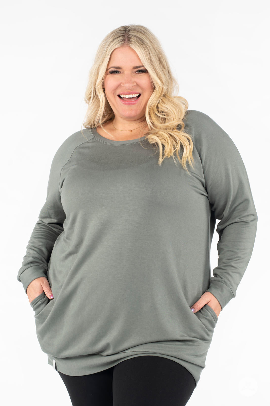 Plus-size model smiling wearing SweetLegs Canada Everyday Raglan Pullover in muted green with hands in pockets and casual pose